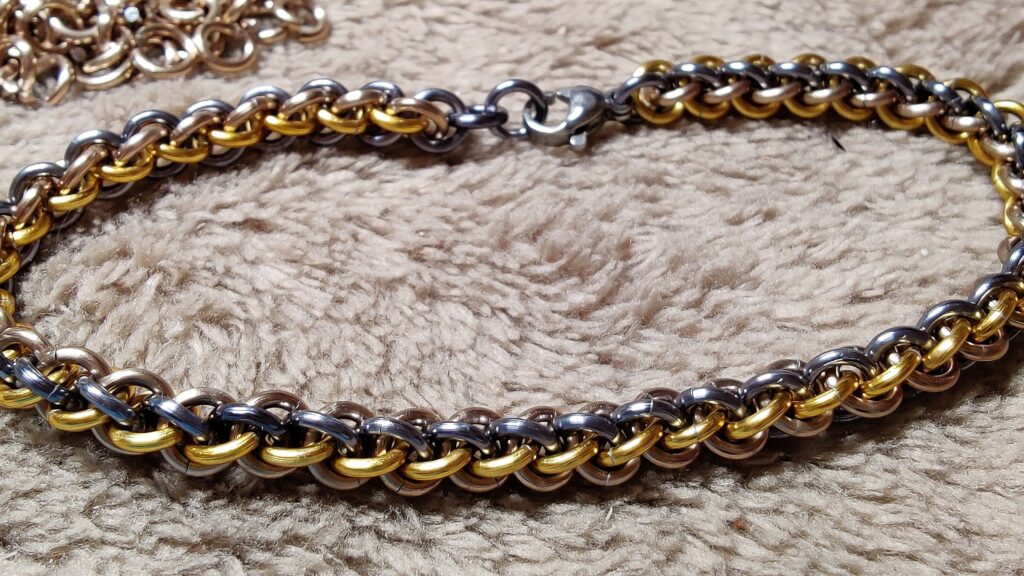 Photo d'un bracelet évoquant une tresse. Il est composé de 3 couleurs : doré, champagne et métal foncé.